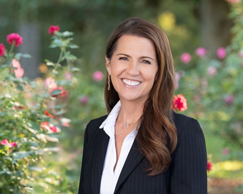 Councilmember Carleen Dark Bays, white woman with dark hair in a white shirt and black blazer smiling with roses behind her.